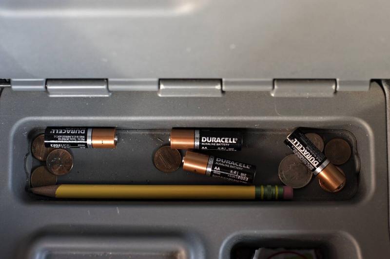 Loose batteries in a container with coins and pencils. 