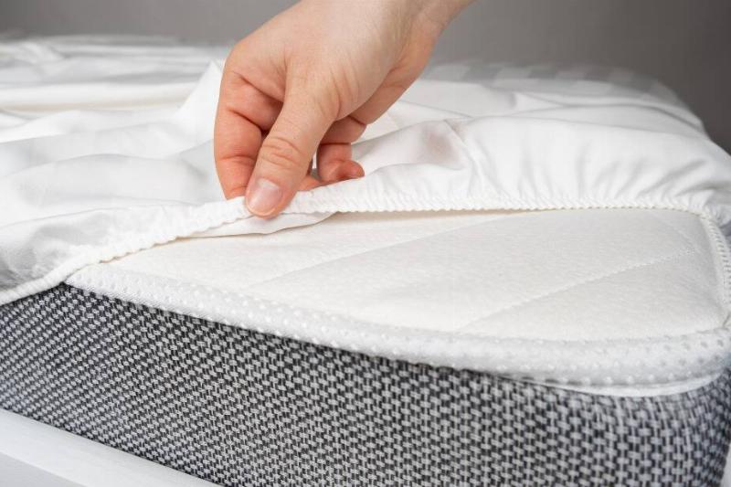 Hands putting fitted sheet on bed. 