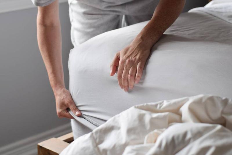 Man putting a sheet on a bed. 