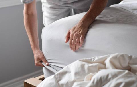 Man putting a sheet on a bed. 