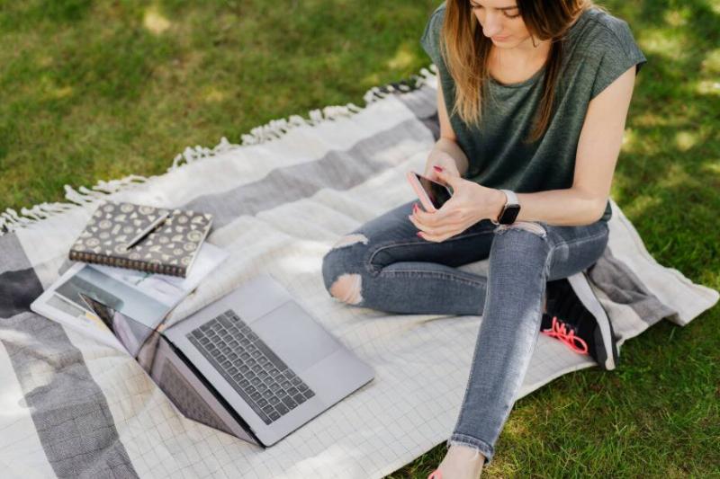 Woman working on laptop on picnic blanket in backyard. 