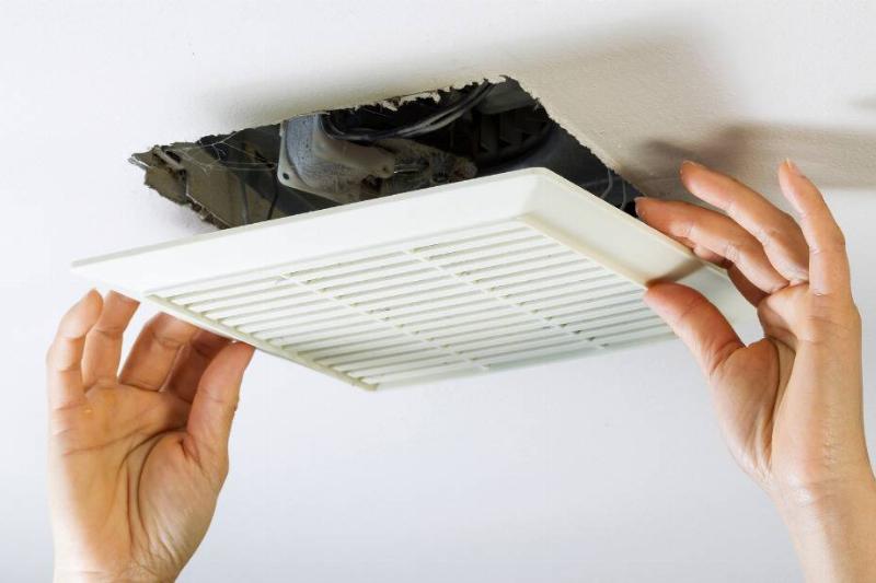 Hands putting exhaust fan back on ceiling. 