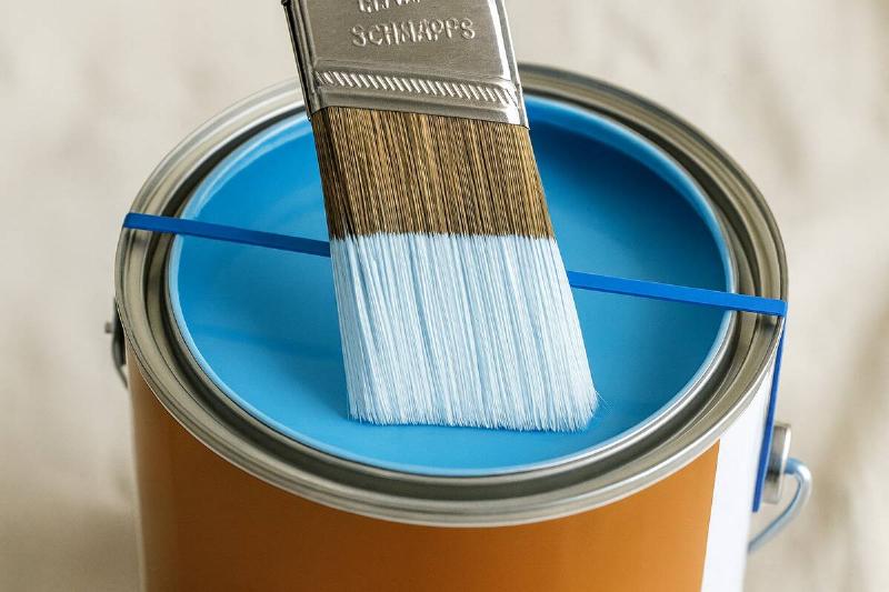 Wiping a paint brush on a rubber band over a paint can. 