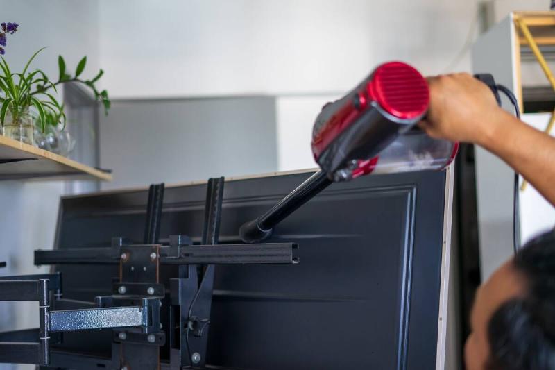 A man vacuum cleaning behind television.
