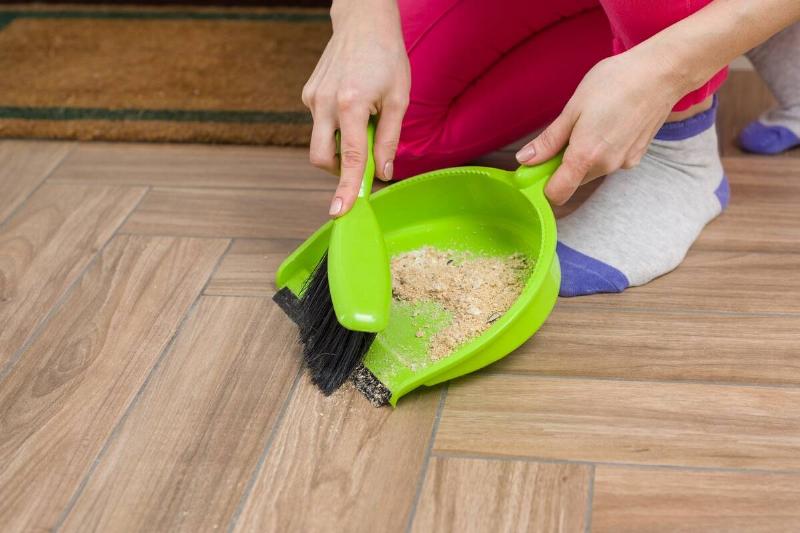Close-up of woman cleaning floor with broom and dust pan.
