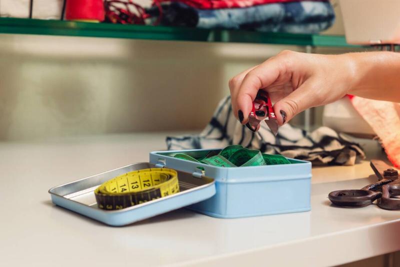 Woman putting sewing stuff in old tin. 