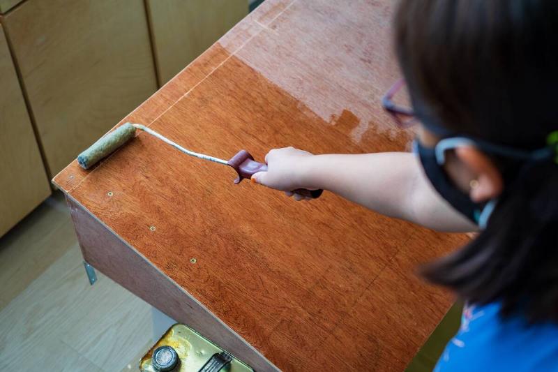 Applying the finish to wood furniture using a hand roller. 
