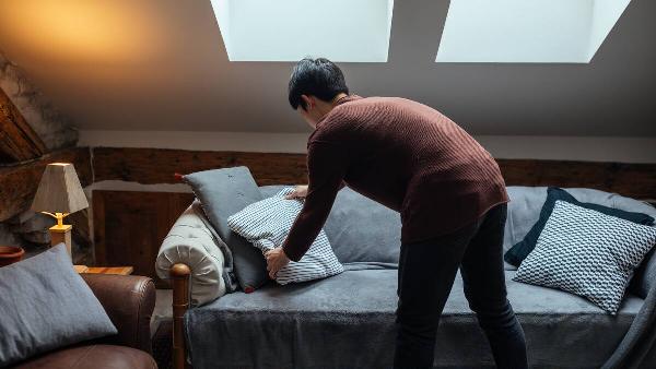 Man rearranging pillows on sofa.