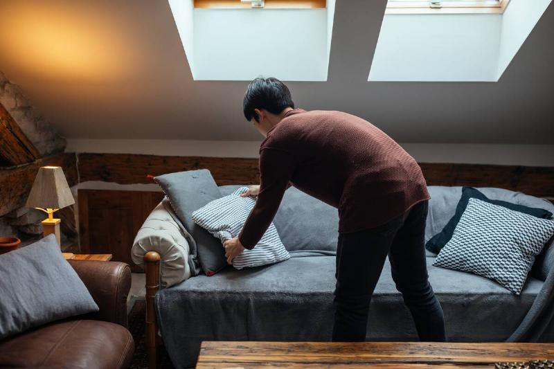 Man rearranging pillows on sofa.