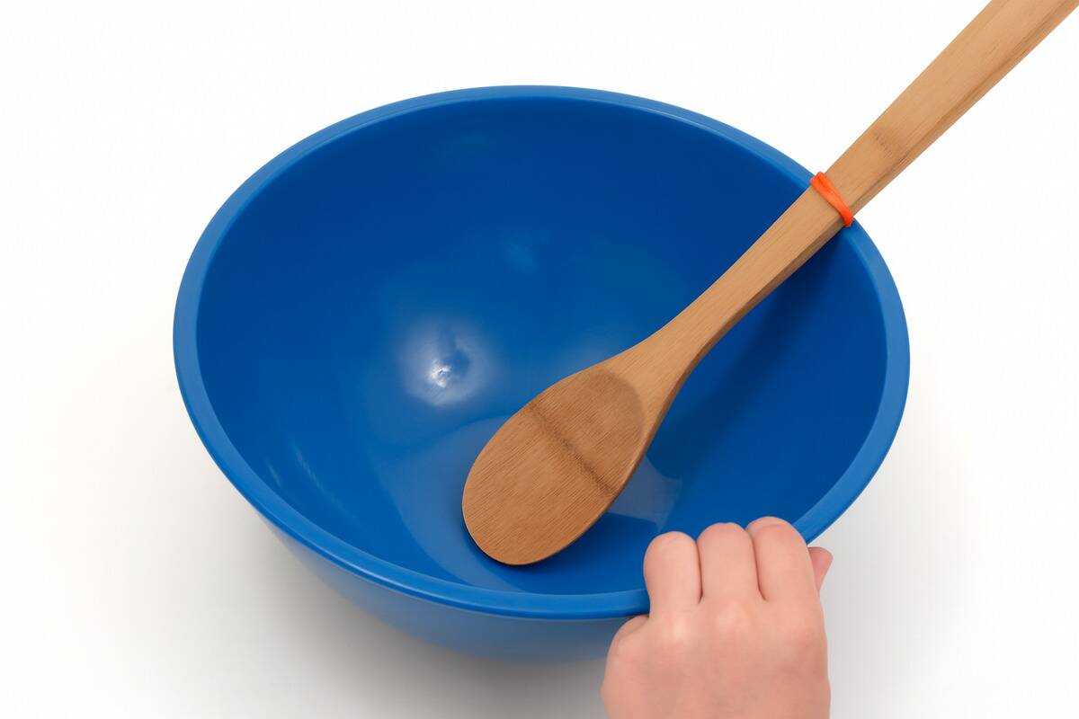 A wooden spoon in a mixing bowl with a rubber band around one end. 