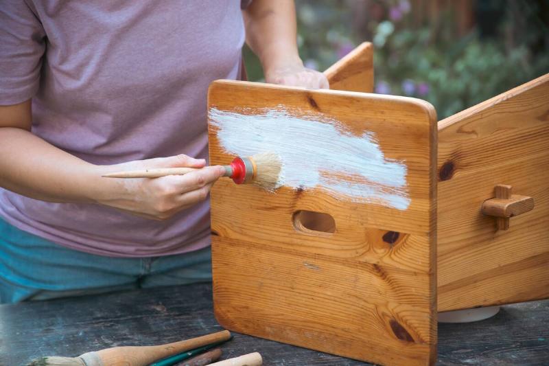 Person painting on a wooden stool. 