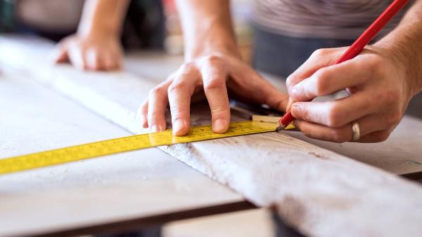 Two people measuring and cutting a piece of wood. 