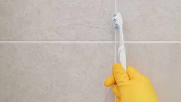 A hand in a glove cleaning grout with a toothbrush.