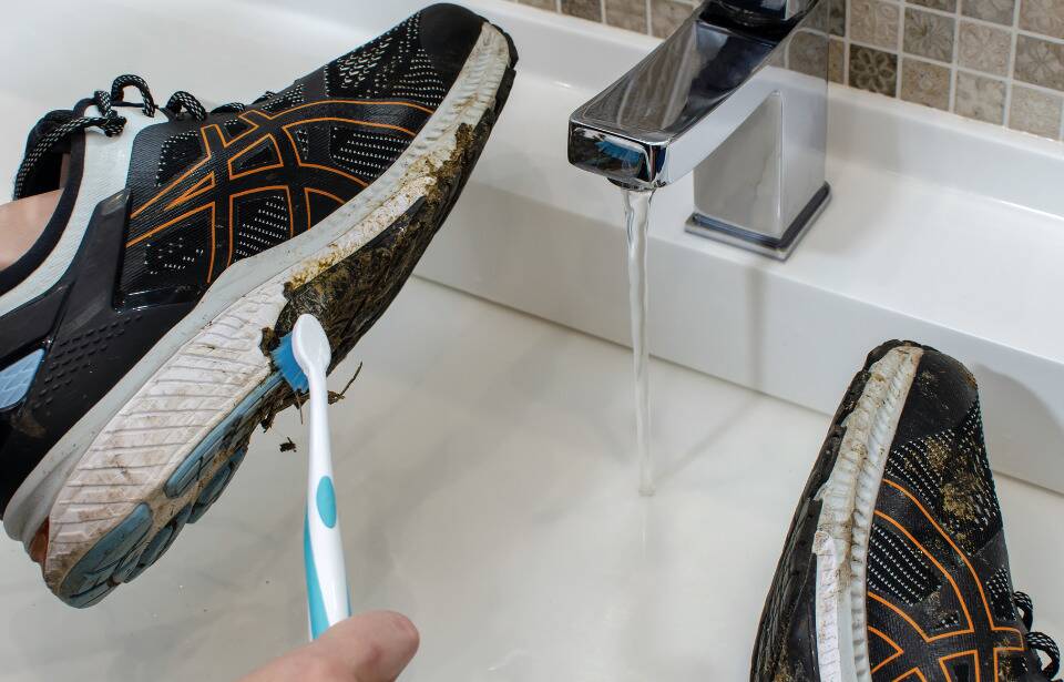 Hands cleaning a sneaker with a toothbrush. 