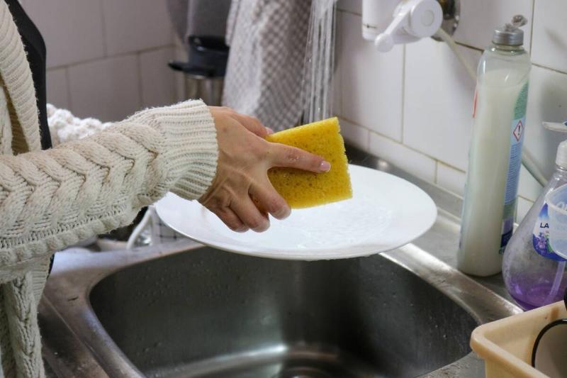 Hands washing dishes with a sponge.