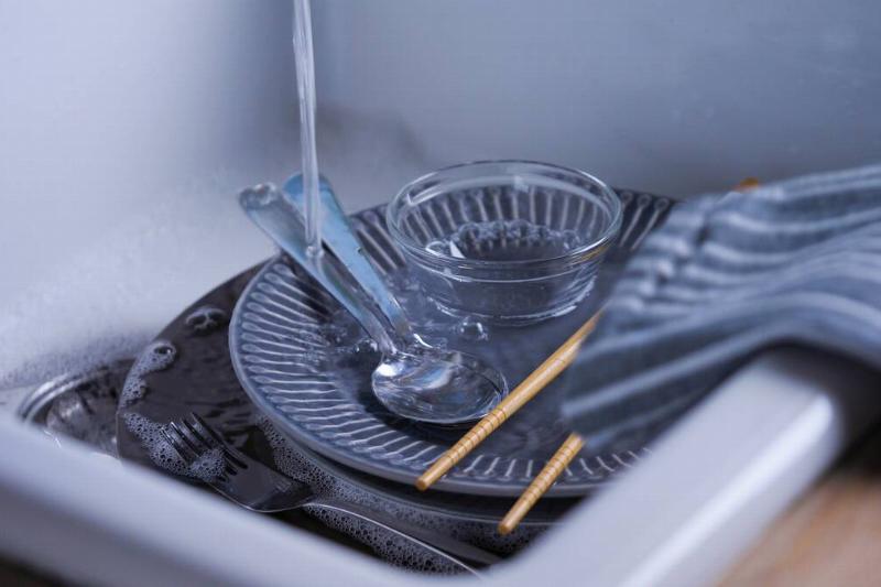 The water streaming on dishes in the kitchen sink.
