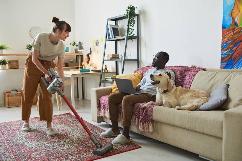 Woman cleaning rug with vacuum with her dog and a man. 