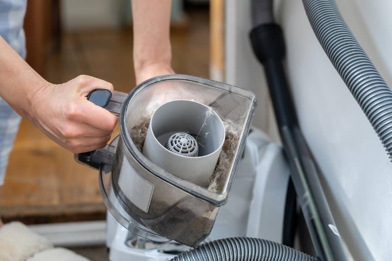 Woman opening dust filter out of vacuum cleaner at home.