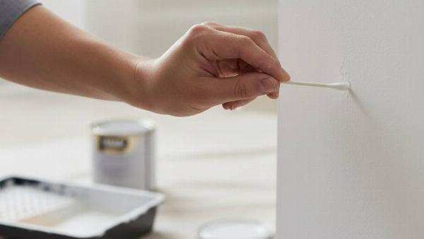 A hand holding a cotton swab and using it to touch up paint on a wall. 