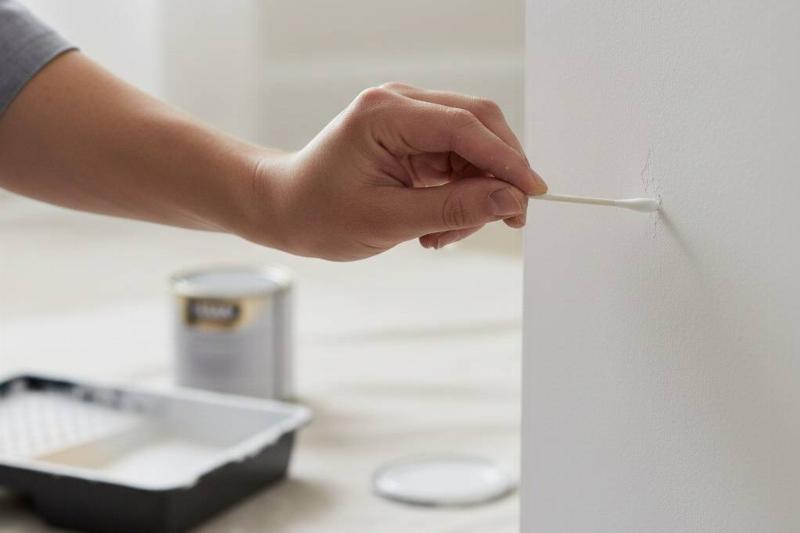 A hand holding a cotton swab and using it to touch up paint on a wall. 