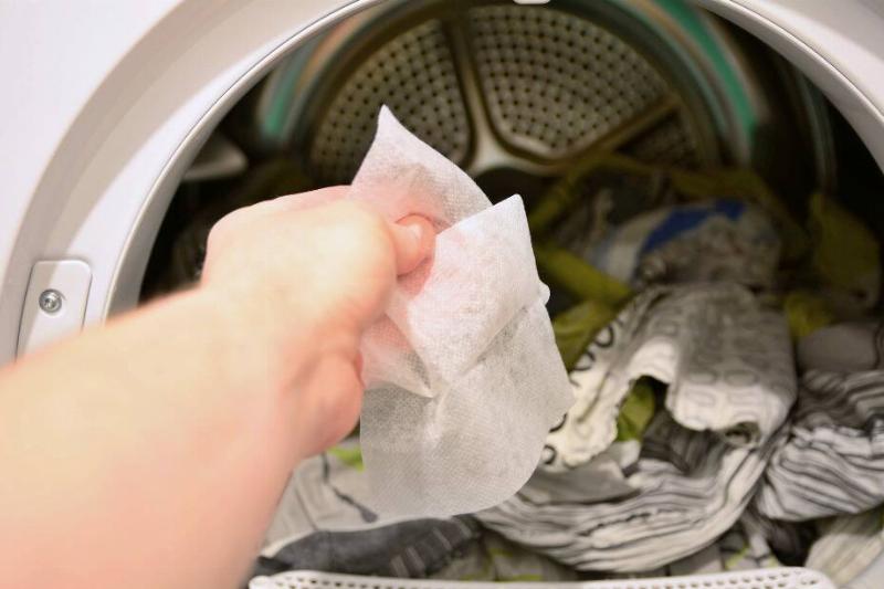 Hand putting a dryer sheet in the dryer. 