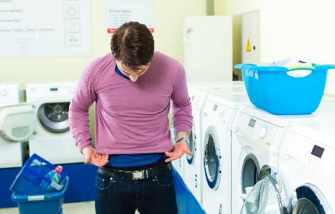 Man putting on shirt he shrunk in the wash. 