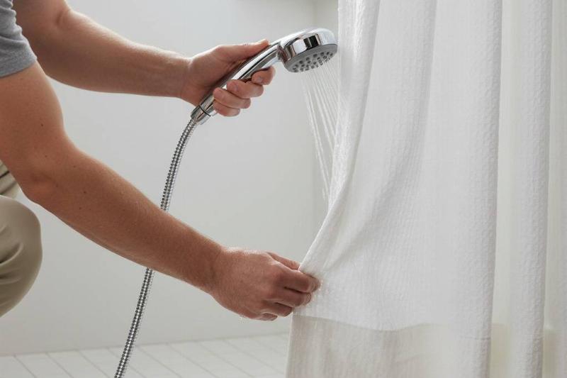 A man rinsing soap off of the bottom of a shower curtain.