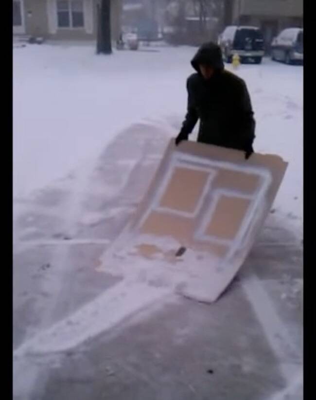 Person pushing snow using a piece of plywood.