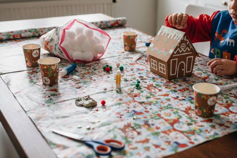 Оберточная бумага-капля. Рождественская оберточная бумага используется для защиты стола, пока ребенок лепит на нем пряничный домик.