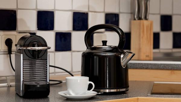 A black kettle, a capsule coffee machine and a mug with a saucer on the kitchen counter.