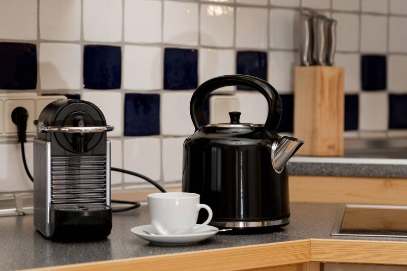 A black kettle, a capsule coffee machine and a mug with a saucer on the kitchen counter.