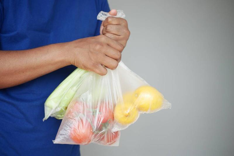 A man holds plastic bags in his hand with vegetables.