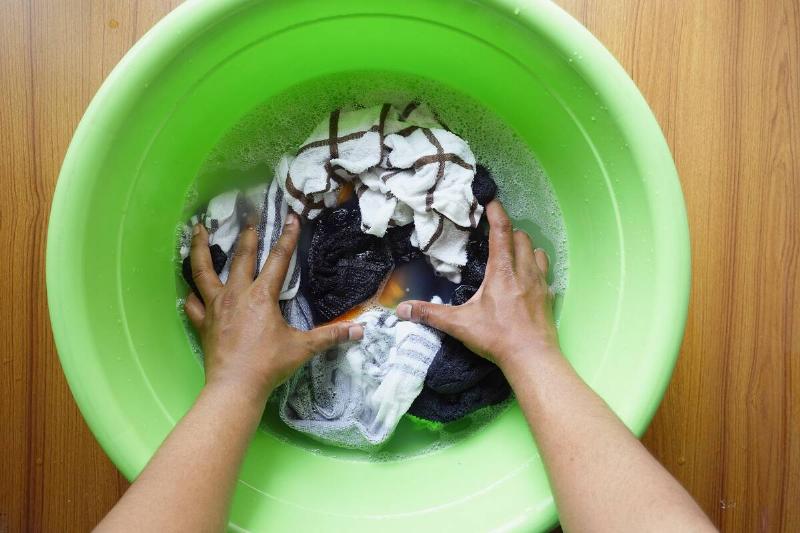 A person soaks clothes in a green bowl with water.