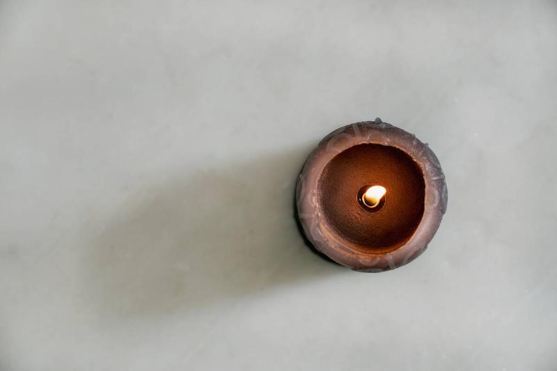 A black candle burning unevenly on a white table. 