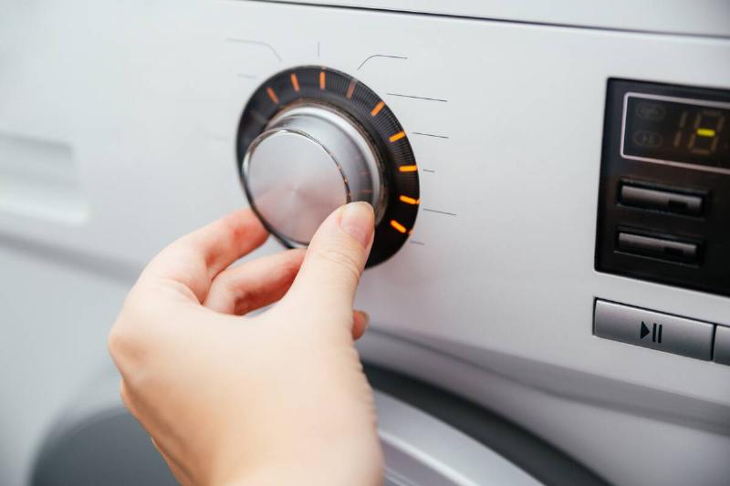 Close-up of a woman's hand on the mode switch of the washing machine.