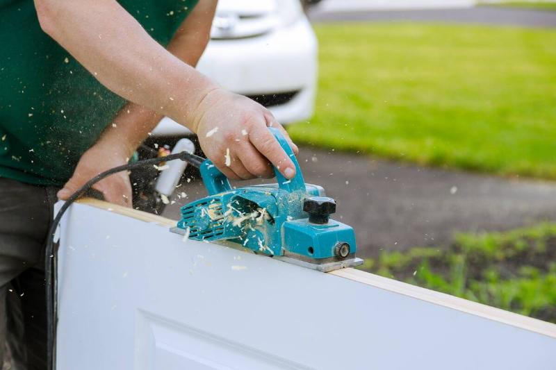 Carpenter using an electric planer on a wooden door. 