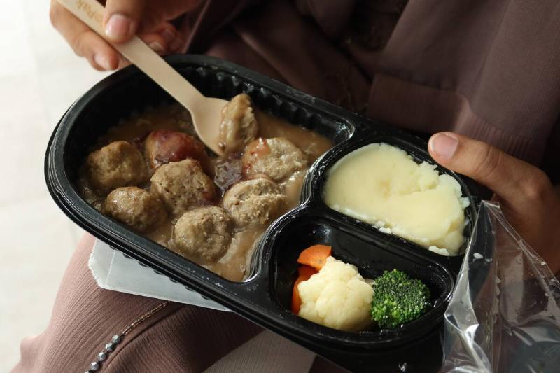 Person eating a frozen meal consisting of meatballs, mashed potatoes and vegetables