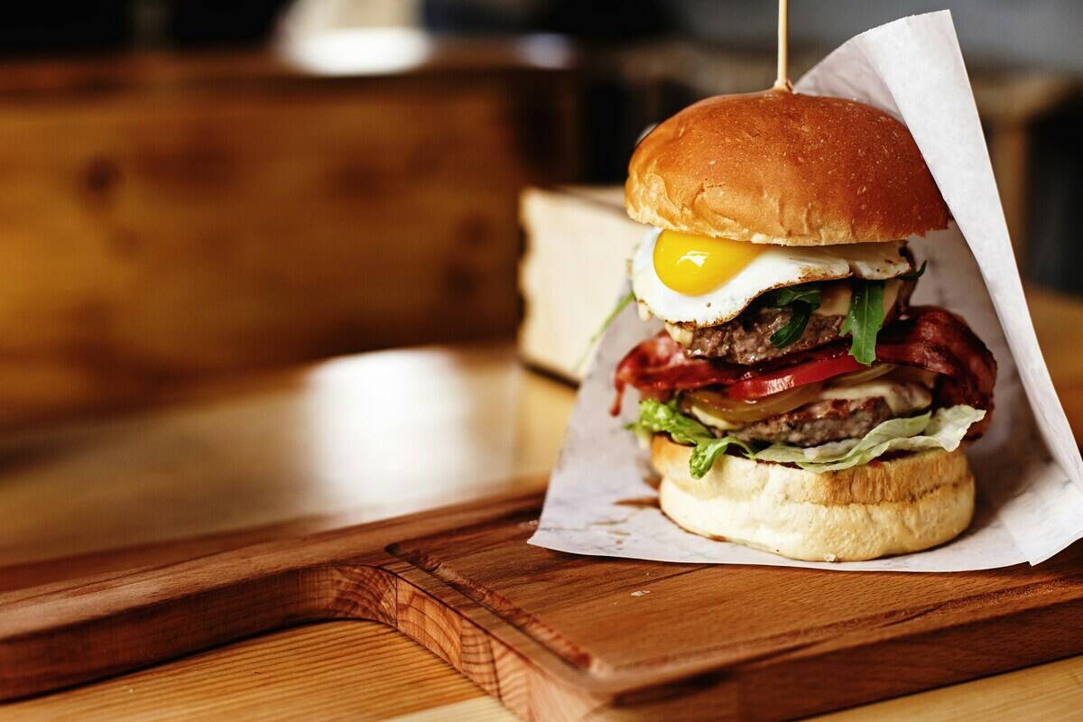 Gourmet burger half-wrapped on a wooden cutting board
