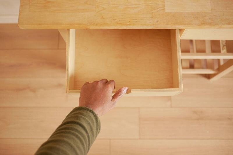 A hand is opening a wooden drawer.