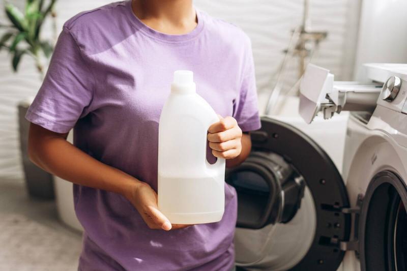 Woman holding vinegar by washing machine.