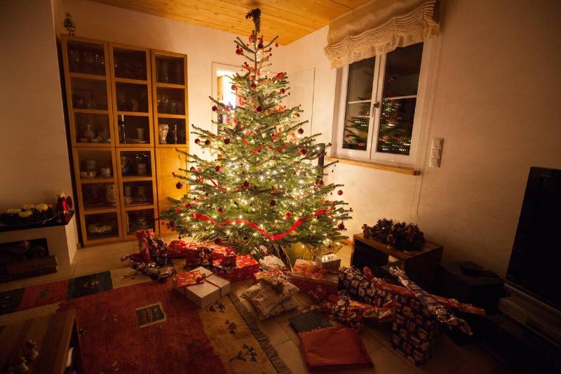 A lot of gifts under the decorated Christmas tree with ornaments and string lights inside a room.