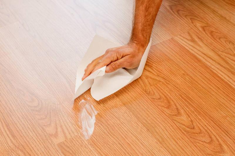Man cleans a damp stain on the wooden floor of his house with absorbent kitchen paper.