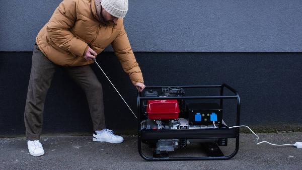 Man in down jacket starting power generator during electricity shutdown.