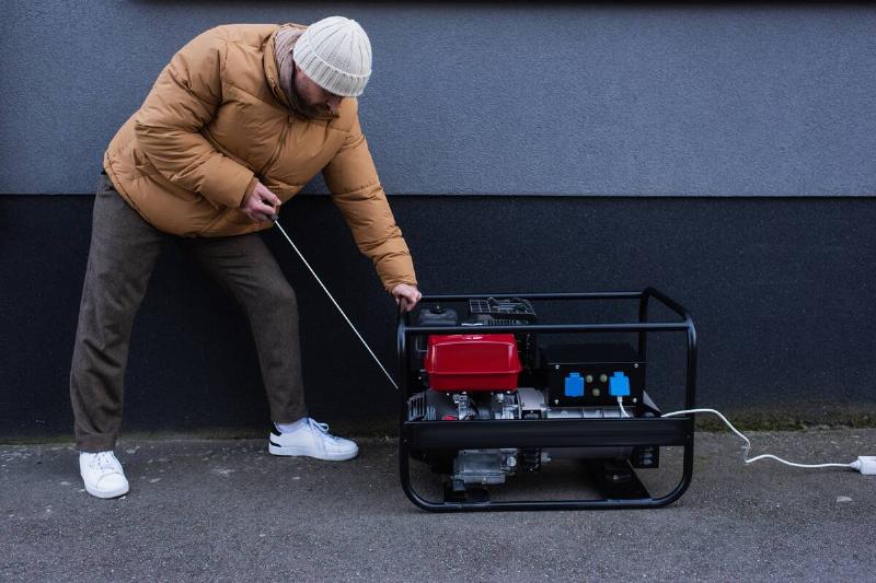 Man in down jacket starting power generator during electricity shutdown.