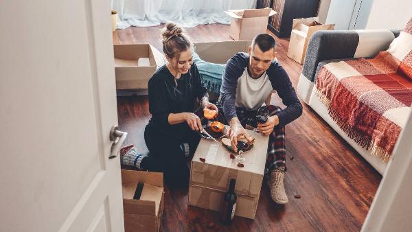 A couple eating off of moving boxes. 
