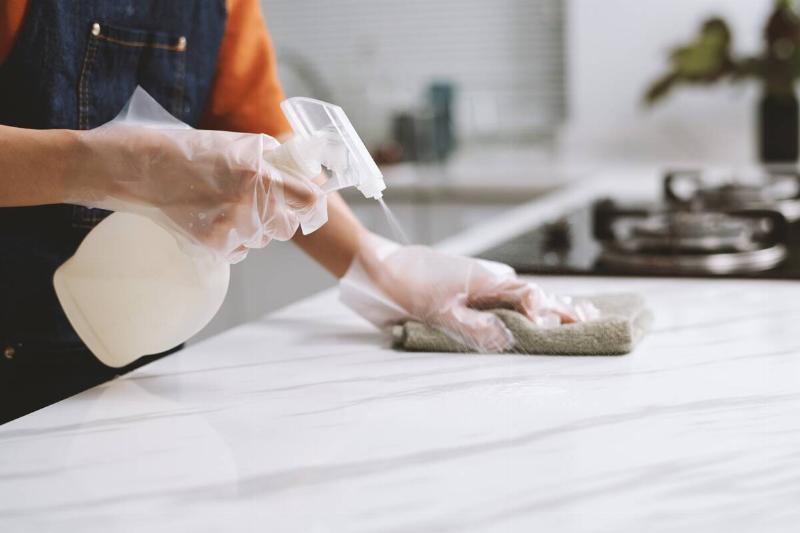 Cropped image of person wearing gloves when cleaning counter with disinfectant spray.
