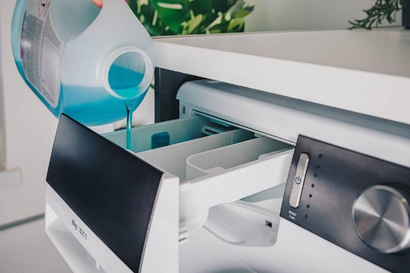 Pouring blue liquid detergent into a washing machine drawer.