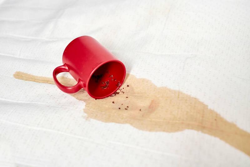A red coffee mug spilled on white cloth. 