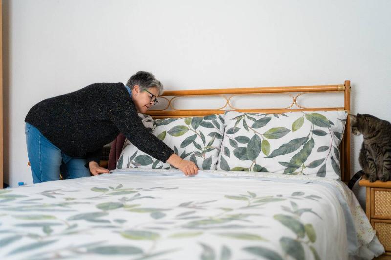 Woman making a bed as a cat watches. 