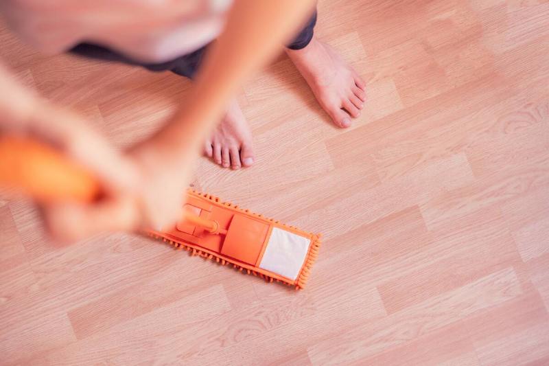 A single man holding a mop and cleaning the laminate floor at home.